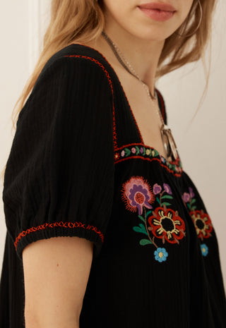 close-up-of-a-woman-wearing-a-black-short-sleeve-top-with-colorful-floral-embroidery-and-red-contrast-stitching-on-the-neckline-and-sleeve-cuffs