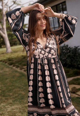 a-woman-wearing-a-black-bohemian-style-maxi-dress-with-a-pink-floral-print-standing-outdoors-in-a-grassy-yard