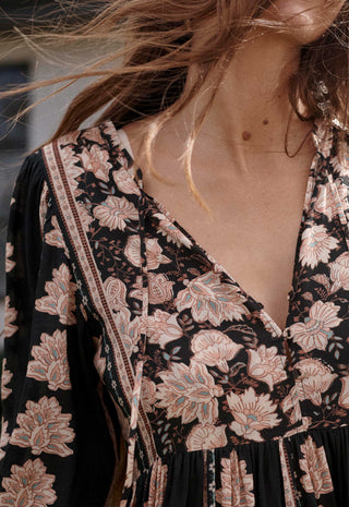 close-up-of-a-woman-wearing-a-black-v-neck-dress-with-a-beige-and-pink-floral-print-styled-with-a-matching-crossbody-bag
