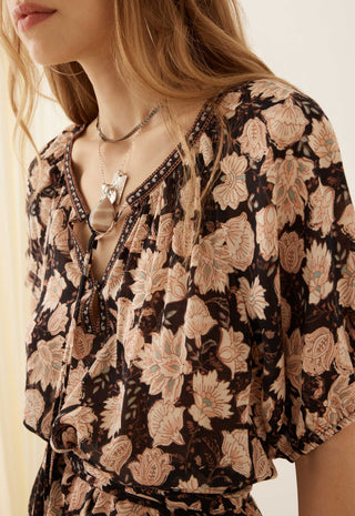 a-close-up-of-a-woman-wearing-a-brown-and-beige-floral-print-blouse-with-a-v-neckline-and-layered-necklaces