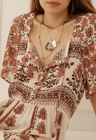 a-close-up-of-a-woman-wearing-a-bohemian-style-cream-dress-with-rust-orange-and-dark-brown-floral-patterns-layered-with-silver-necklaces